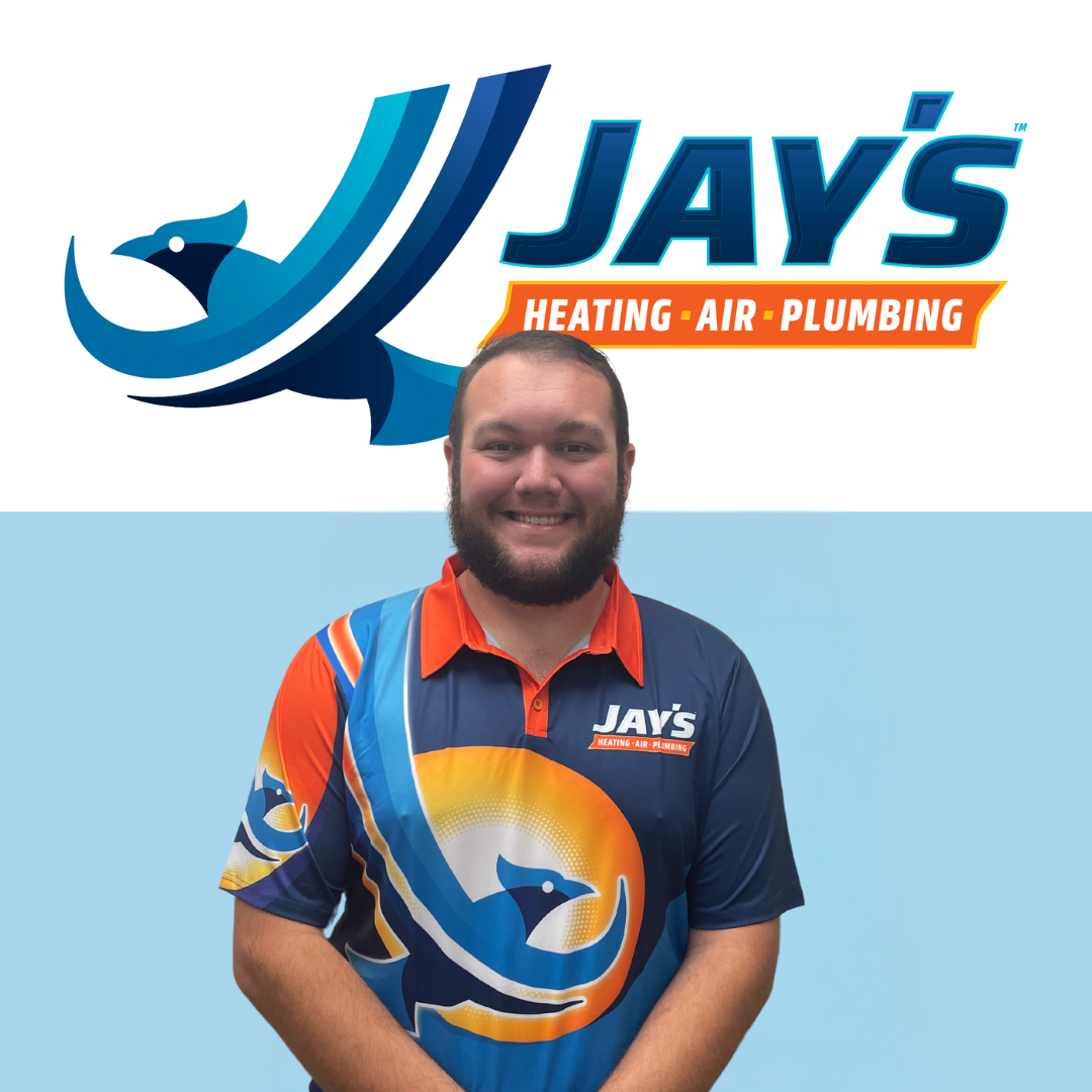 A team member wearing a Jay’s Heating, Air, Plumbing shirt stands proudly in front of the company logo adorned with a blue bird design.